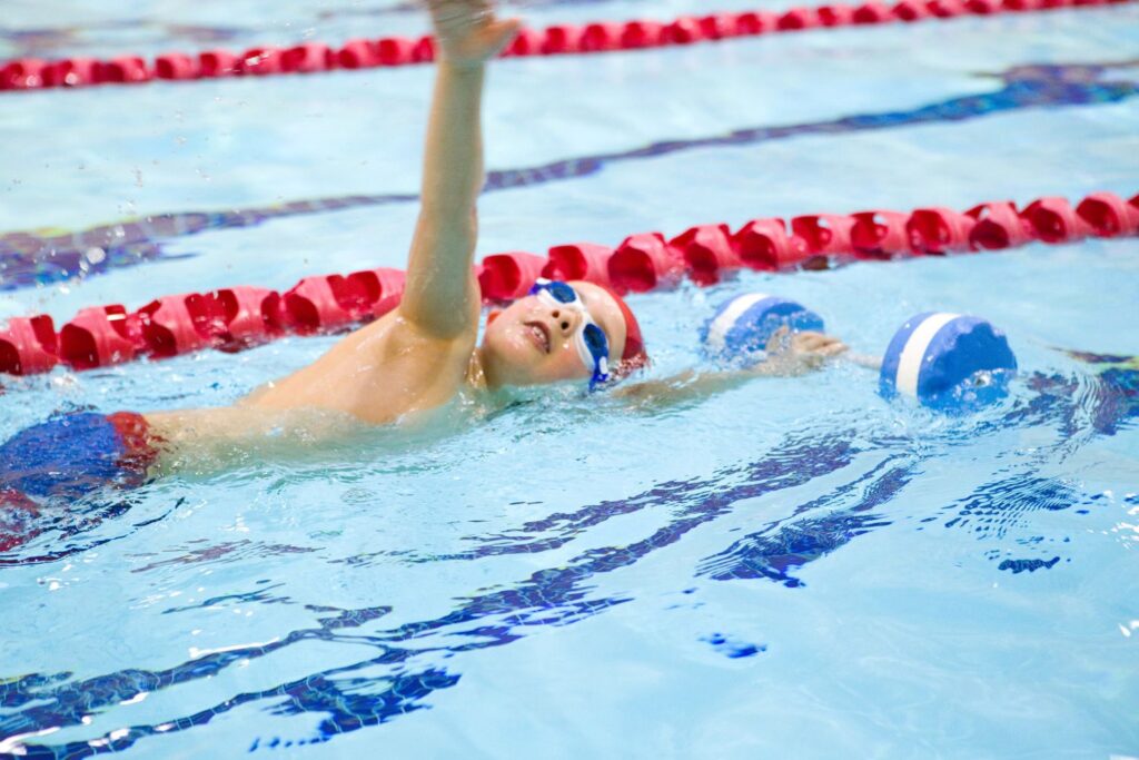 Young child swimming in a pool wearing earplugs during a beginner swim lesson