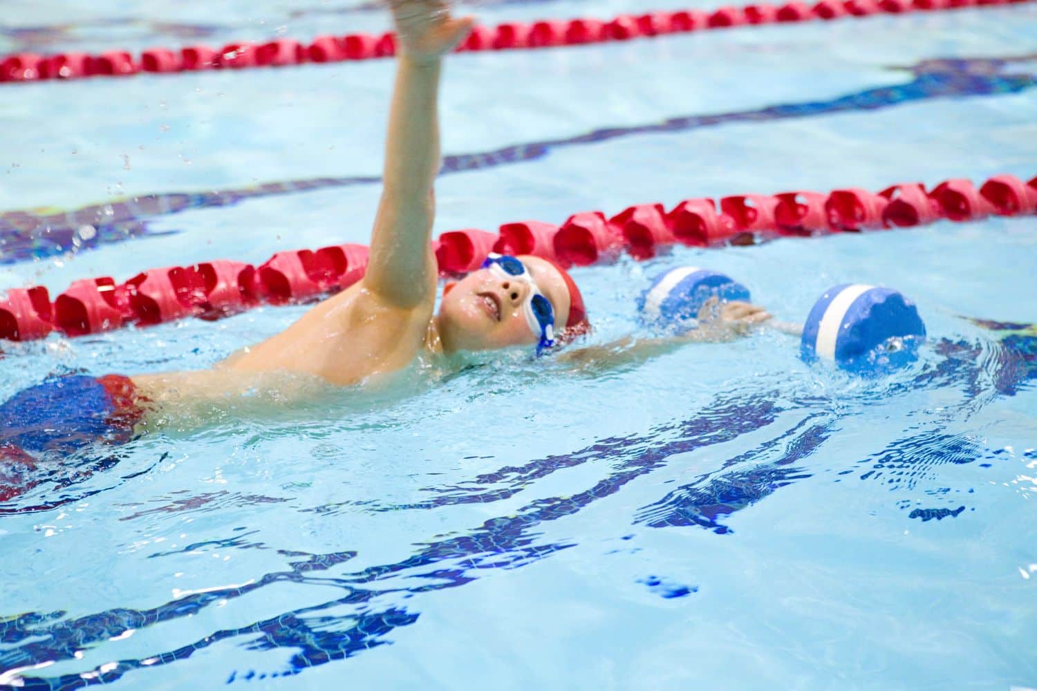 Young child swimming in a pool wearing earplugs during a beginner swim lesson, freestyle swimming technique
